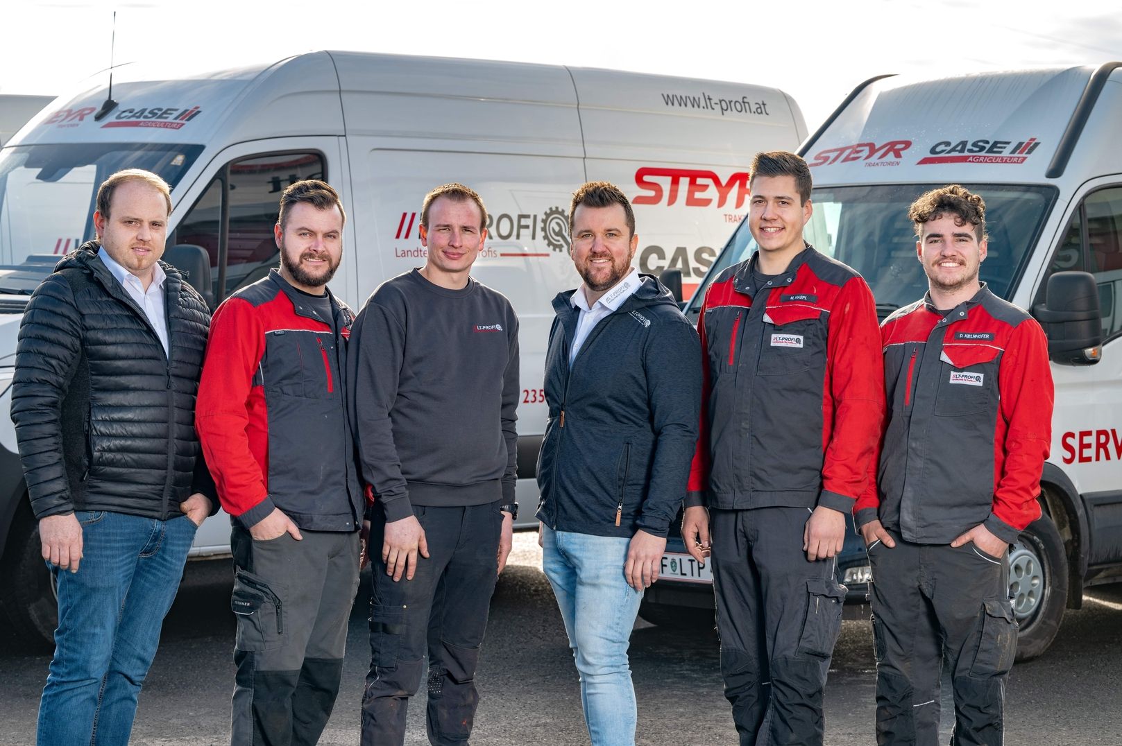 Eine Gruppe von sechs Männern in Arbeitsuniformen posiert gemeinsam vor Servicewagen