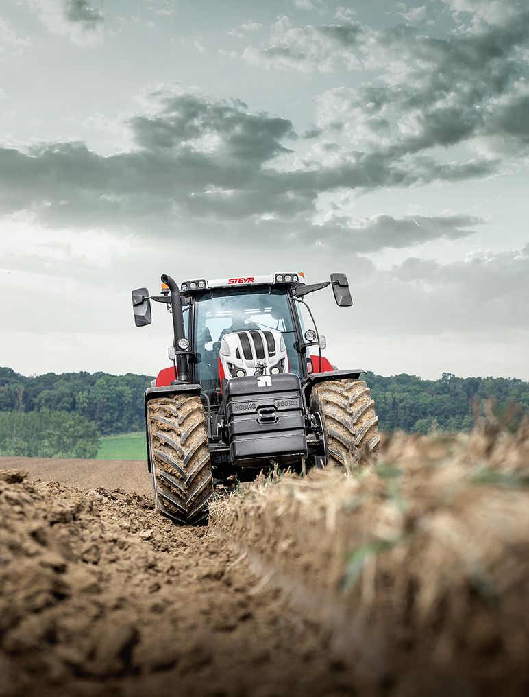 Ein rot-schwarzer Traktor pflügt unter bewölktem Himmel ein Feld